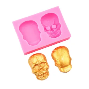 Detail view of pink silicone skull mold with two golden skull casts on white background