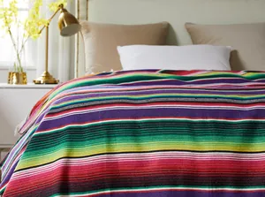 Colorful Mexican striped serape blanket detail on a cozy bed with warm room lighting