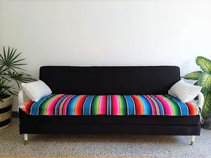 Colorful Mexican serape table runner with fringe shown as a decorative sofa cover throw