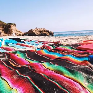 Close-up detail of a colorful Mexican striped woven blanket spread on a sunny beach sand