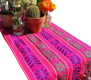 Vue détaillée des motifs tissés vibrants sur un chemin de table mexicain rose avec glands.