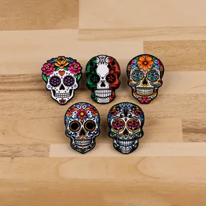 Close-up detail view of five colorful Mexican sugar skull enamel pins on a natural wood surface