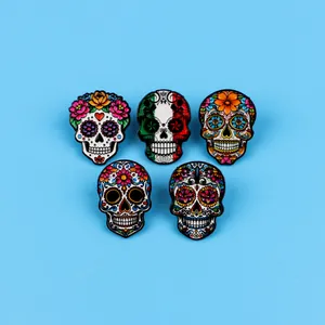 Detailed view of five colorful Mexican sugar skull enamel pins on a blue background