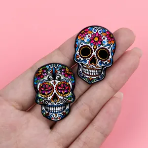Detailed view of two colorful Mexican sugar skull enamel pins against a pink background