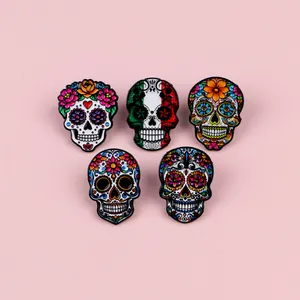 Detailed view of five colorful Mexican sugar skull enamel pins set on a pink background