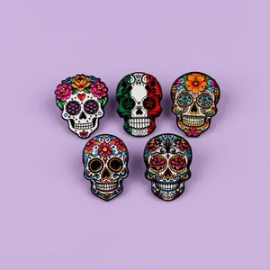 Five colorful Day of the Dead Mexican sugar skull enamel pins on purple background