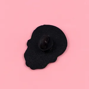 Close-up detail showing the back of a black skull enamel pin with a rubber clutch.