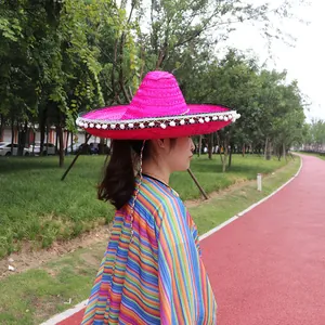 Detail view of a bright pink Mexican straw sombrero with pom-pom trim on a model