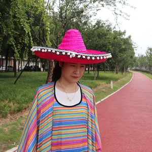 Pink Mexican straw hat with white pom-poms worn by a model in an outdoor setting