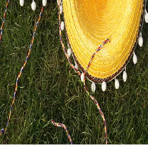 Detailed view of yellow Mexican straw hat with white pom-poms and colorful ropes