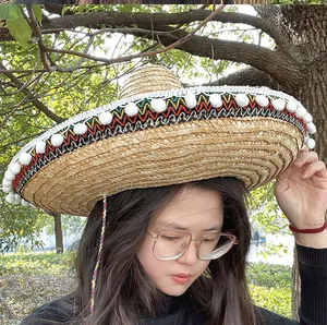 Detailweergave van een strooien Mexicaanse sombrero met borduurwerk en witte pompons.