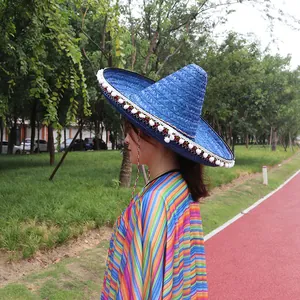 Detail view of blue straw Mexican sombrero with white pom-poms and rainbow poncho