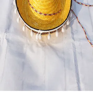 Detailed view of yellow Mexican straw hat with white pom-pom trim and colored cord