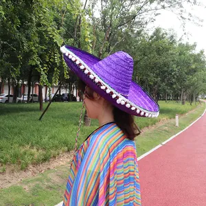 Detail of a vibrant purple Mexican straw sombrero with white pom-pom trim on a model.