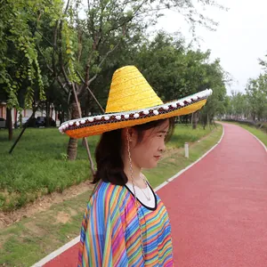 Adult wearing a yellow Mexican straw sombrero with decorative white pom-poms in a park