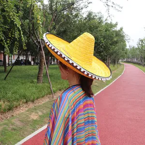 Detail view of a yellow Mexican straw hat with white pom-poms in an outdoor setting
