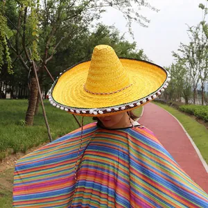Detailed view of yellow Mexican sombrero hat with white pom-poms and striped poncho