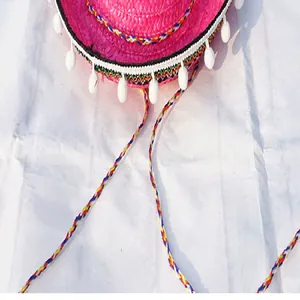 Detail view of pink Mexican straw hat with white tassels and colorful braided strap