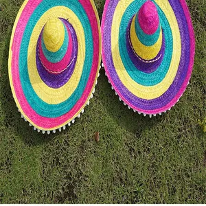 Close-up of colorful straw woven Mexican sombrero hats with pom-pom trim on grass.