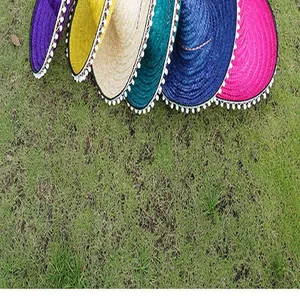 Detailed view of colorful Mexican straw hats with pom-poms on green grass lawn
