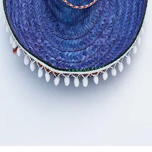 Detail view of a blue straw carnival hat with white pom-poms and colorful braided trim