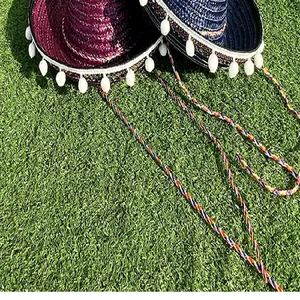 Close-up detail of purple and navy blue Mexican straw hats with white pompoms on green grass