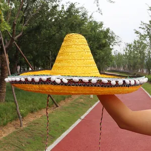 Detail of a bright yellow straw Mexican sombrero with white pom-pom trim and ethnic band.