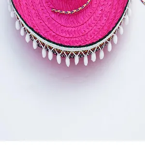 Detail view of pink Mexican straw hat with white pom-pom trim and colorful band