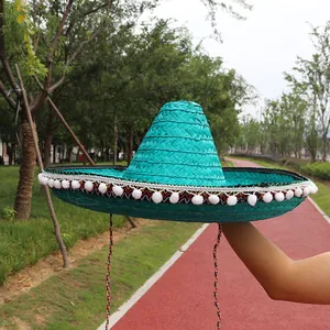 Detailed side view of a vibrant turquoise Mexican straw hat with white pom-pom fringe decoration