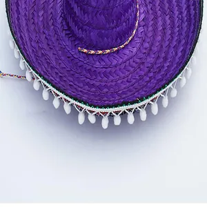 Macro view showing the fine braided texture of a purple Mexican straw hat with white pom-poms