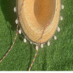 Close-up detail of Mexican straw sombrero with white pompoms and colorful braided strap.