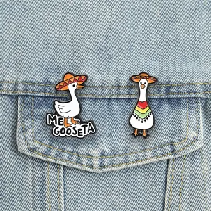 Detailed macro view of two funny Mexican goose enamel pins pinned to a light blue denim jacket