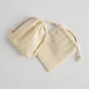 Zwei kleine beige Kordelzugbeutel aus Baumwolle für Schmuck, einer mit Inhalt.
