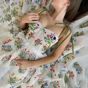 Elegantes weißes Netzkleid mit bunter Blumenstickerei und grünen Samtträgern zum Binden.