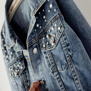 Close-up of a blue denim jacket detailing elegant pearl embellishments and metal buttons