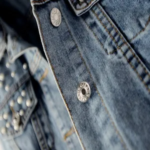 Close-up detail of blue denim jacket featuring pearl beads and engraved metal buttons.