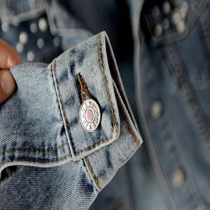 Close-up detail of denim jacket cuff with metal button and beaded embellishments