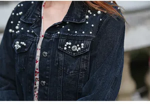 Detailed close-up of white pearl and bead embellishments on a dark denim jacket