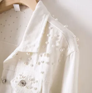 Detailed close-up of a white denim jacket featuring elegant pearl and rhinestone accents.