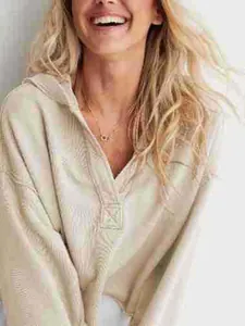 Lächelndes Model in einem beigen Kapuzenpullover mit V-Ausschnitt und Textur
