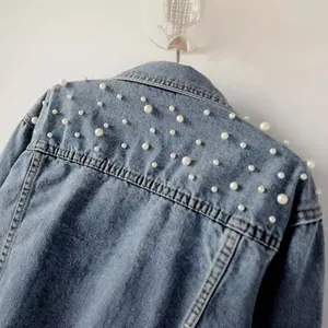 Detail view of white pearl bead embellishments on the shoulder of a blue denim jacket