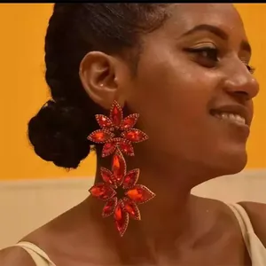 Close-up view of luxury oversized red crystal flower drop earrings worn by a model