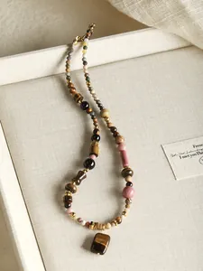 Gros plan d'un collier en œil de tigre et agate naturelle sur lin beige.