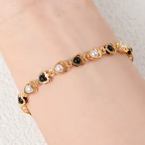 Detail view of a gold-tone heart-shaped bracelet with elegant black and white pearls