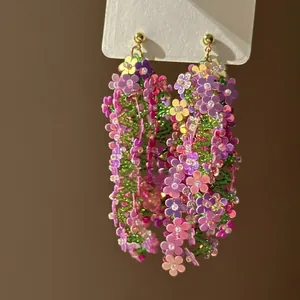 Handmade woven flower earrings with colorful petals and green beads for holiday style.