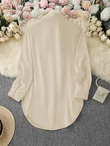 Back view of a long-sleeved beige women's blouse with an asymmetrical curved hem.