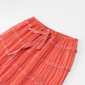 Dettaglio della gonna lunga a pieghe color corallo con bordo in pizzo e coulisse
