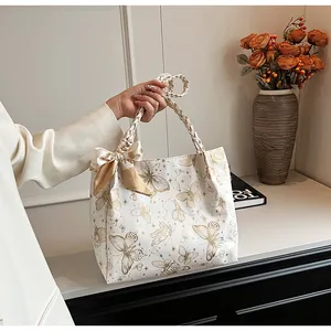 Detailweergave van een witte draagtas met vlinderprint, gevlochten handvatten en strik