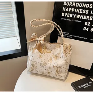 Detailweergave van een witte draagtas met gouden vlinderprint en een gevlochten riem