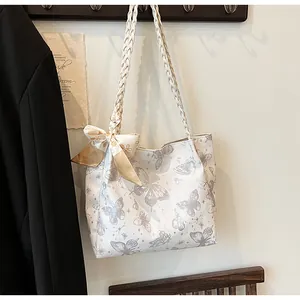 Detail van de witte tote tas met vlinderprint, gevlochten hengsels en zijden strik